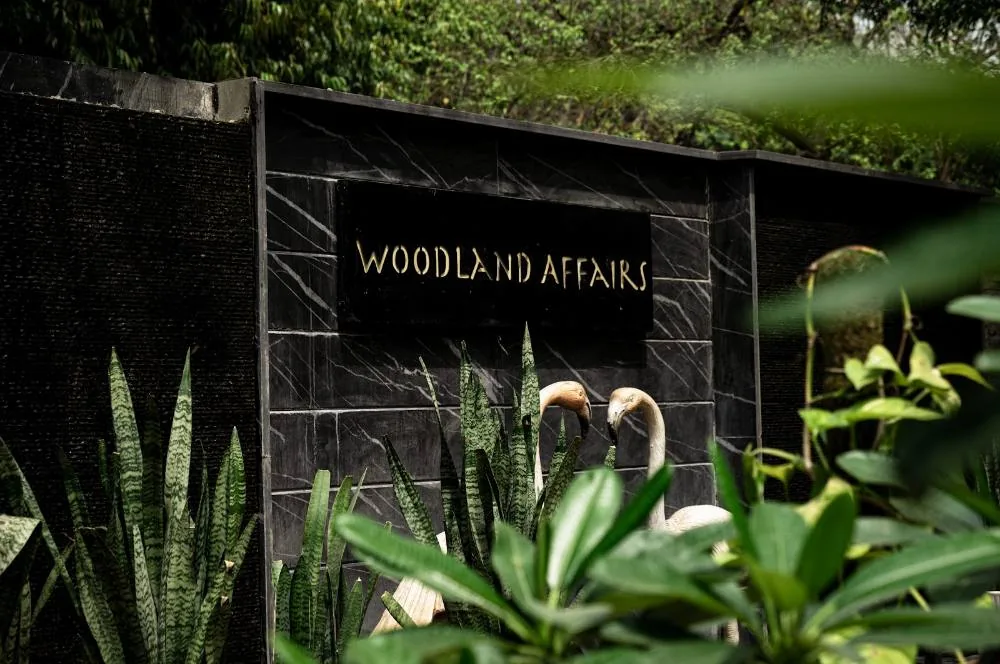 The Woodland Affairs signage wall, half-hidden in a wall of foliage.