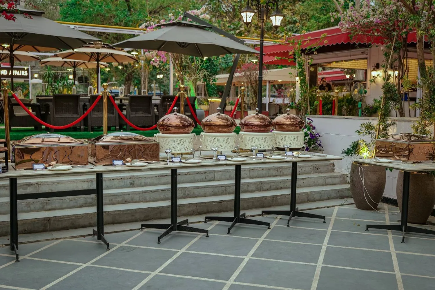 As the light softens, the courtyard warms up — lamps on, umbrellas open, the garden at its best.